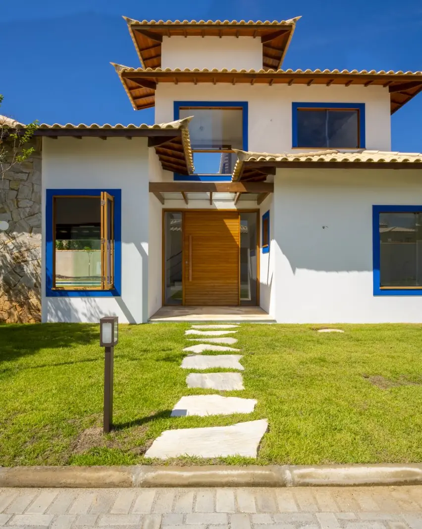 Fachada de uma residência do Paineiras, com porta de madeira, esquadrias azuis e pedra