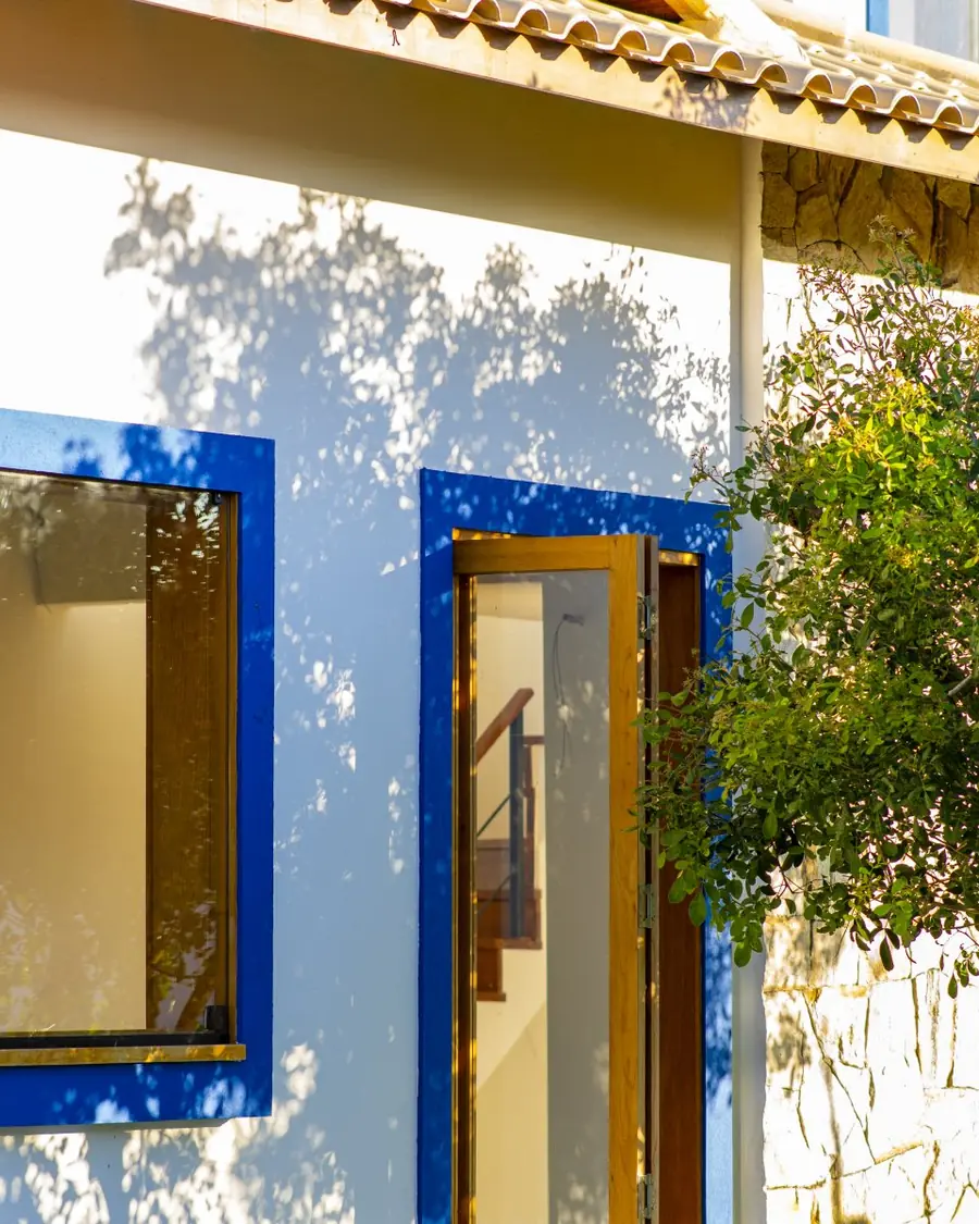 Detalhe da fachada com esquadria azul, madeira e parede de pedra
